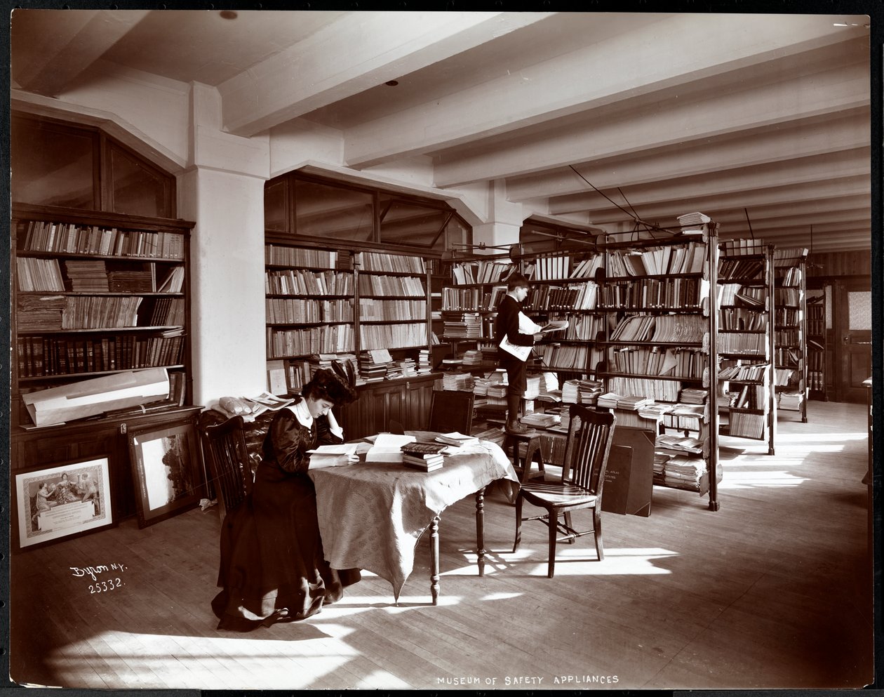 Frau und ein junger Mann in einer Bibliothek des Museums für Sicherheitsgeräte des American Institute of Social Service, New York, 1907 (Silbergelatineabzug) von Byron Company