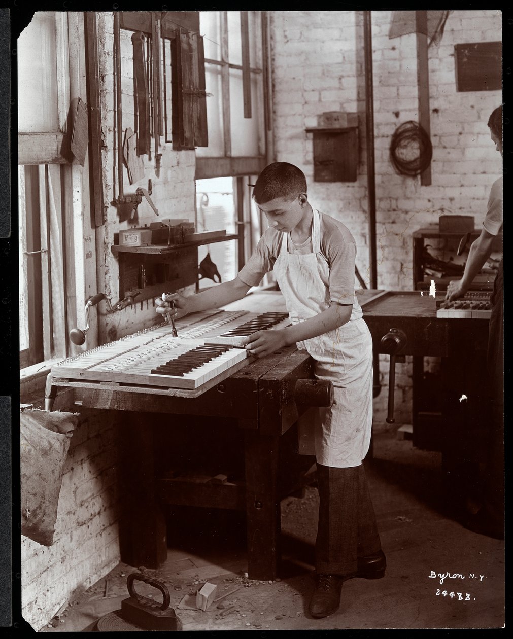 Ein junger Mann arbeitet in der Harrington Piano Co. Fabrik, 1907 (Silbergelatineabzug) von Byron Company