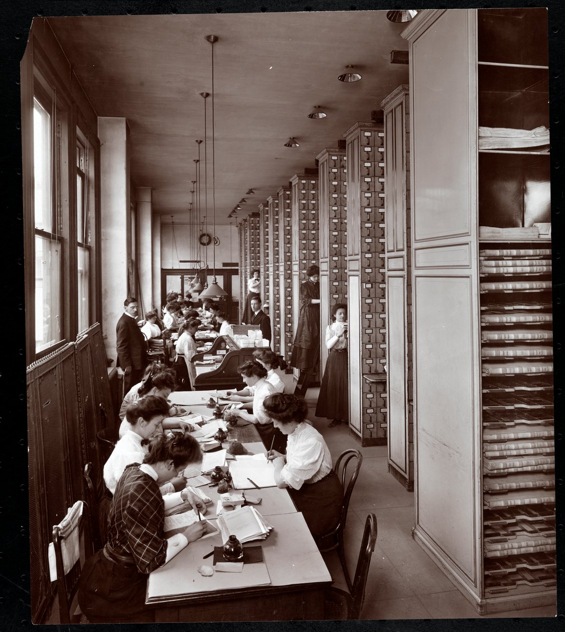 Frauen arbeiten in einem Aktenraum, unter männlicher Aufsicht, bei der Metropolitan Life Insurance Co. in der 23rd Street und Madison Avenue, New York, 1907 von Byron Company