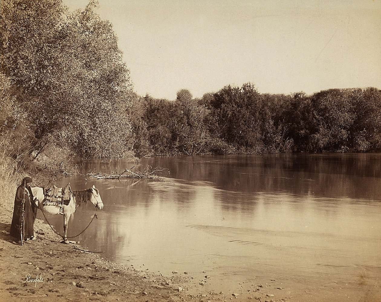 Ein Mann in traditioneller Kleidung mit seinem Pferd vor einem See in Ägypten von Félix Bonfils