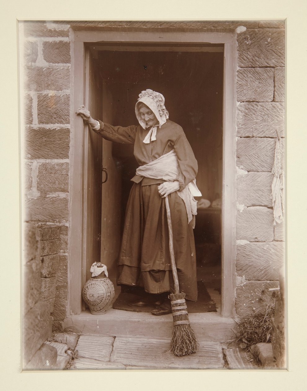 Eine alte Dame mit einer Hefeflasche an einer Hüttentür von Frank Meadow Sutcliffe