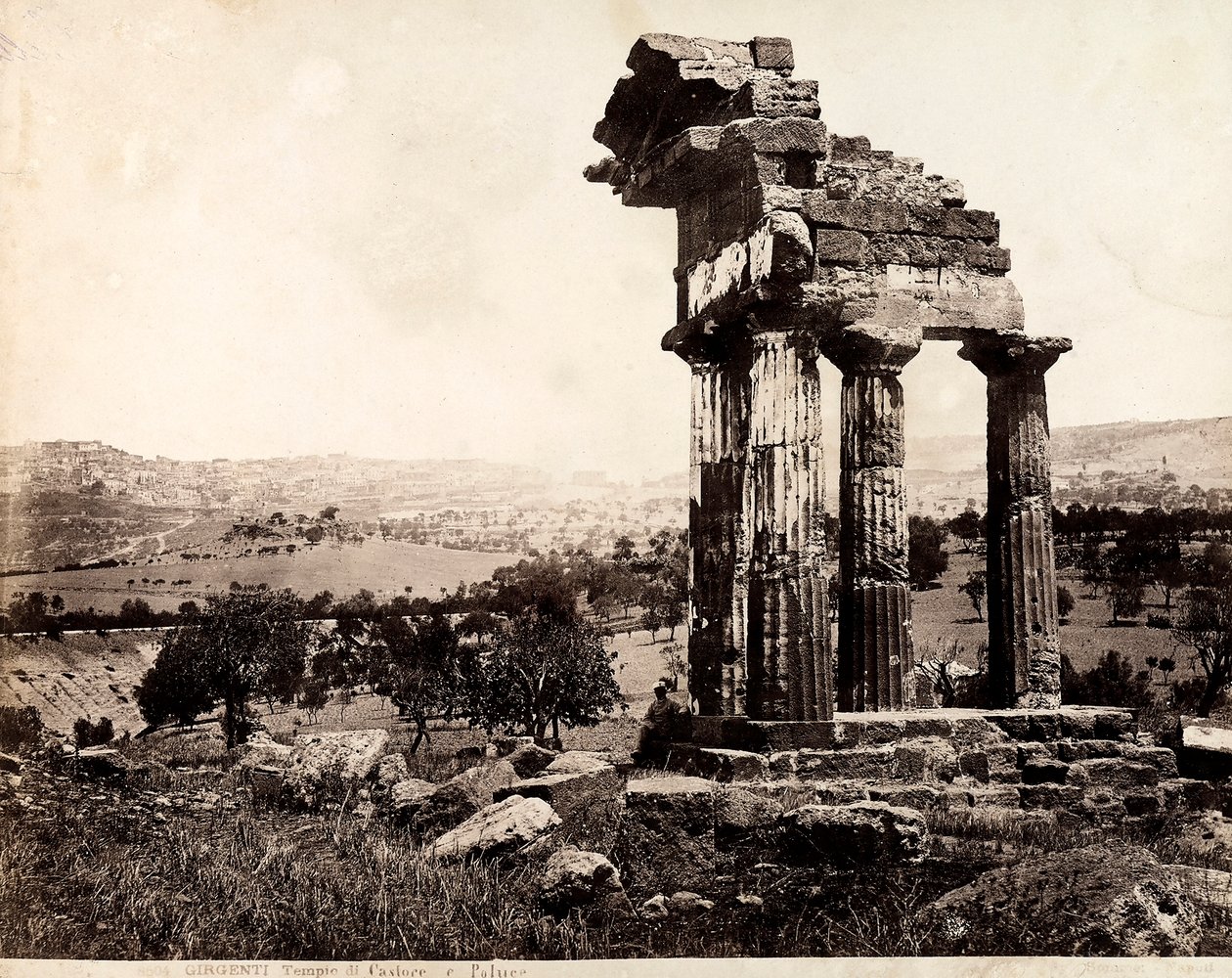 Ansicht der verbleibenden vier Säulen, die ein Gebälk des Tempels von Castor und Pollux im Valle dei Templi, Agrigent, tragen. Im Hintergrund ist ein Panorama der Stadt sichtbar von Giorgio Sommer