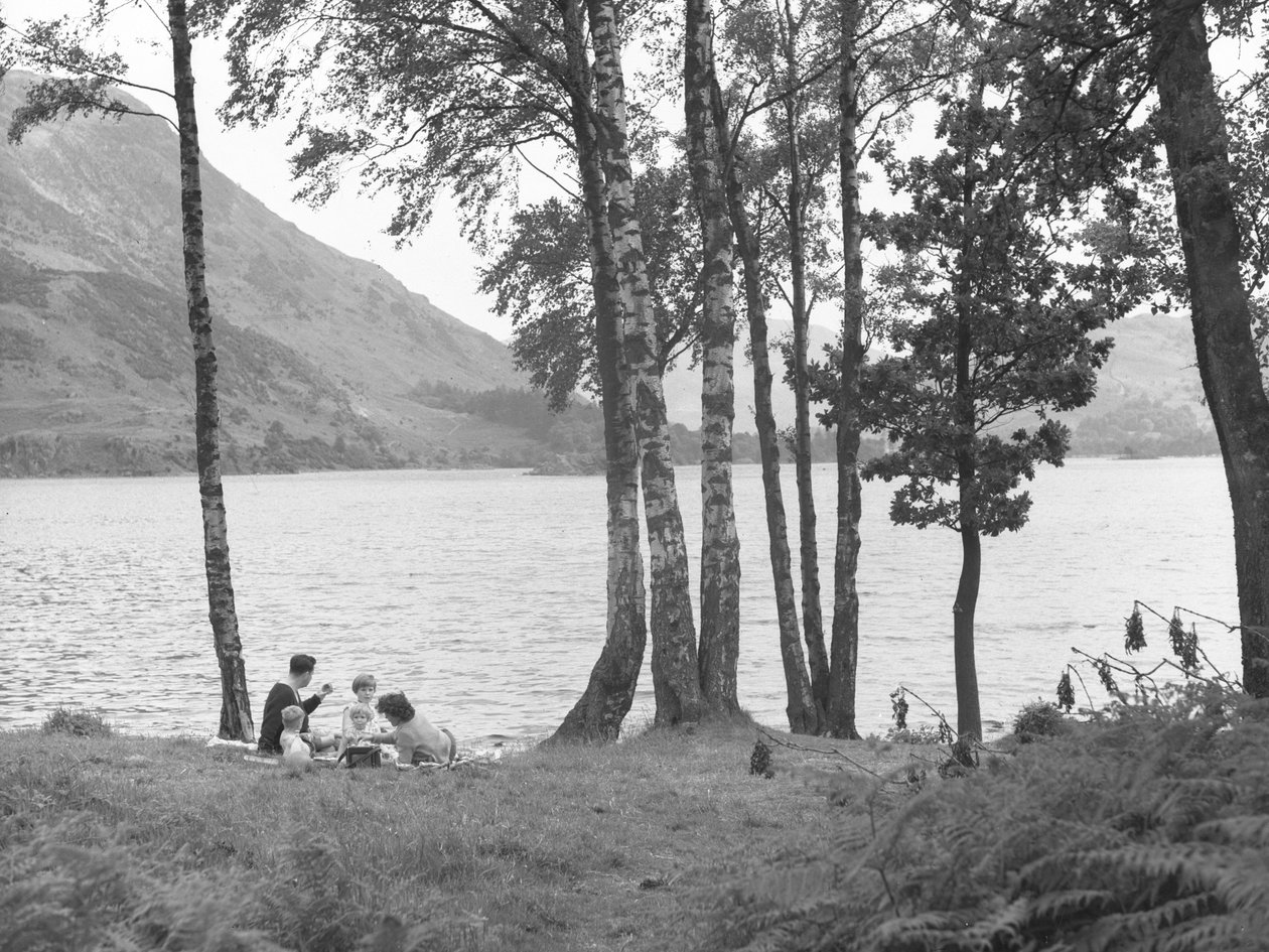Eine Familie entspannt sich in der Nähe eines Sees mit Bäumen rechts und Hügeln im Hintergrund von Joseph Hardman