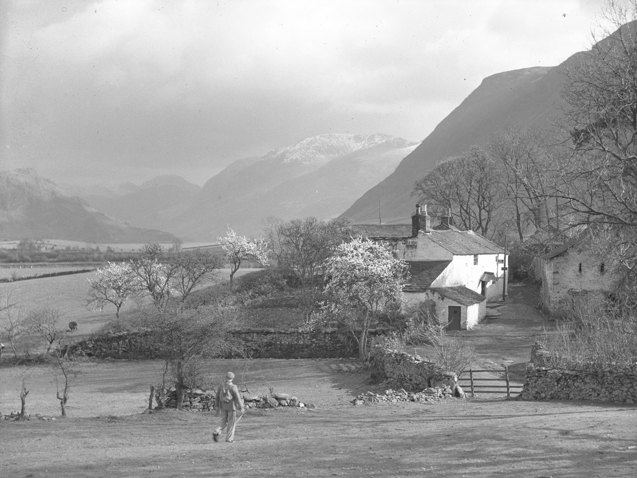 Ein Mann geht auf einen Weg und Gillerthwaite House zu, mit See und Hügeln im Hintergrund von Joseph Hardman