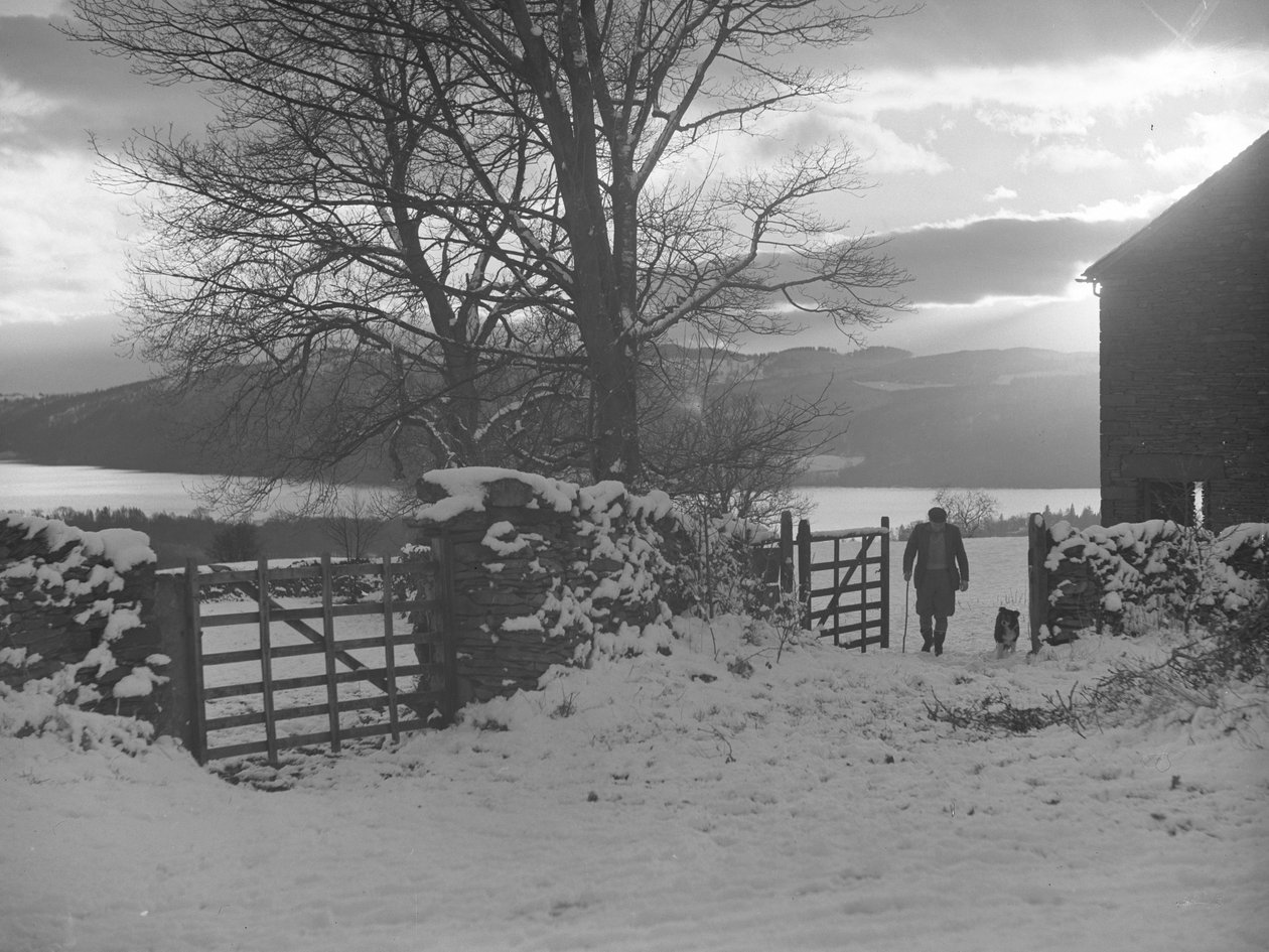 Mann und Hund gehen durch ein Tor zur Kamera im Schnee mit Thirlmere dahinter von Joseph Hardman