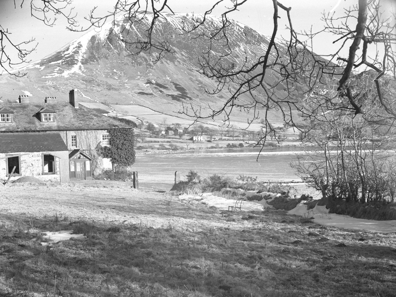 Das Anglers Hotel in Ennerdale mit Bäumen im Vordergrund und gefrorenem See und verschneiten Hügeln dahinter von Joseph Hardman
