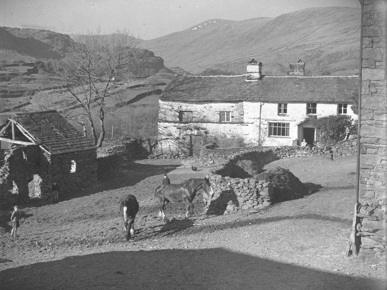 Drei junge Jungen beobachten Pferde im Bauernhof in Kentmere mit Bauernhaus und Hügeln dahinter von Joseph Hardman