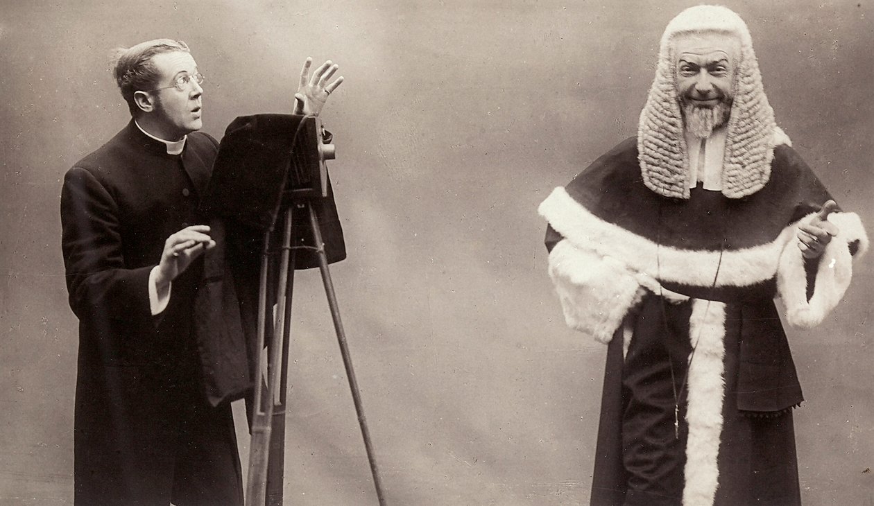 Ein Mann in Soutane richtet die Linse seiner Kamera auf einen Mann, der wie ein Papst gekleidet ist von Rotary Photographic Co Ltd