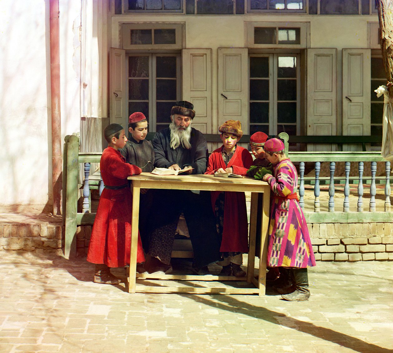 Eine Gruppe jüdischer Kinder mit einem Lehrer auf einem Tisch vor einem Haus, Samarkand, Russisches Reich, zwischen 1905 und 1915 von Sergey Prokudin Gorsky