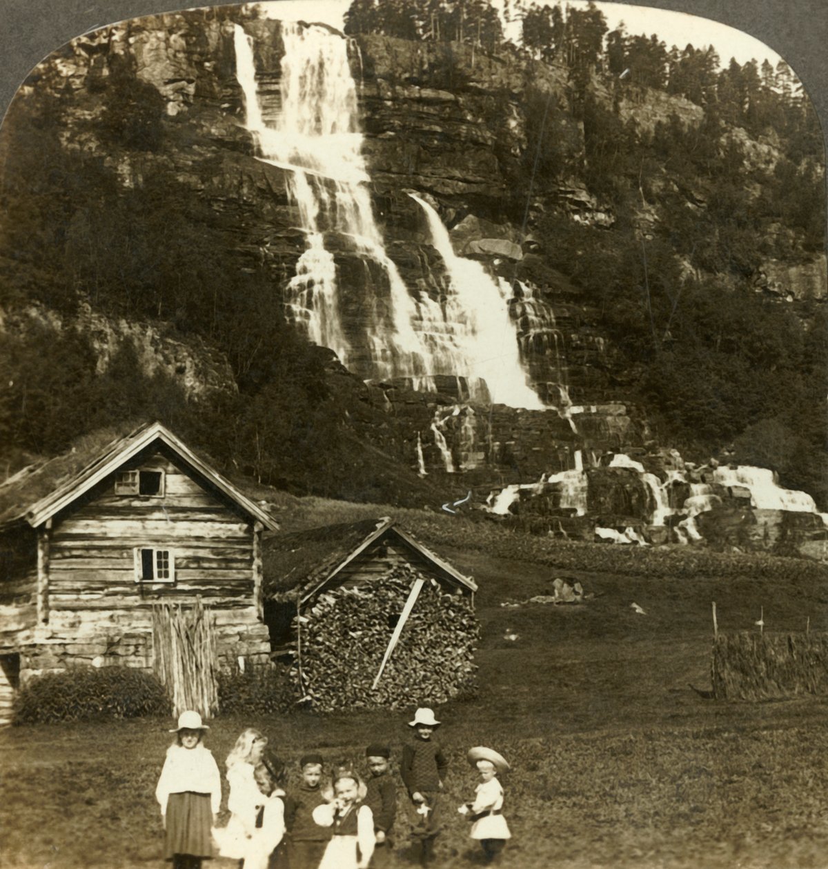 Kinder spielen auf einem Bauernfeld mit terrassiertem Tvinde-Wasserfall, Vossevangen, Norwegen von Unbekannt