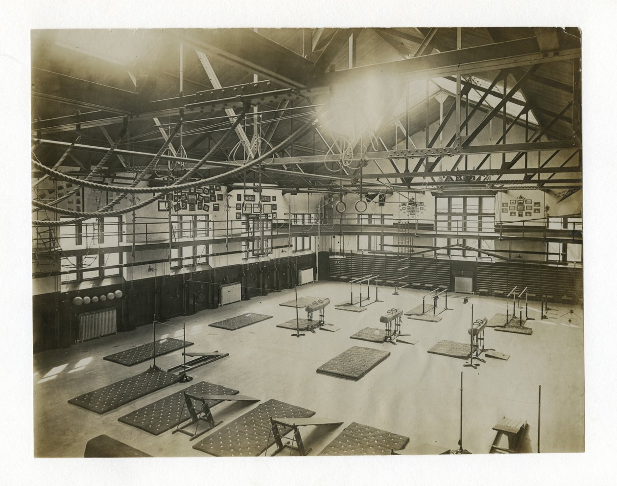 Horizontales Foto des Inneren einer großen Turnhalle. Geräte und Matten sind auf dem Boden verteilt von Unbekannt
