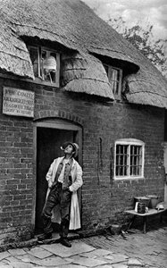 Ein Mann raucht eine Pfeife vor einem Geschäft, Worcestershire, um 1922 von A. W. Cutler