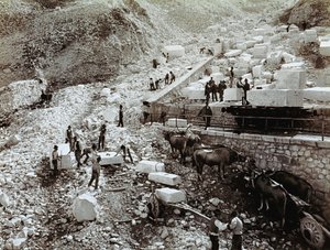 Bahnhof mit Arbeitern, die Marmorblöcke auf Eisenbahnwaggons laden, drei Ochsenpaare mit Transportwagen sind sichtbar (s/w Foto)