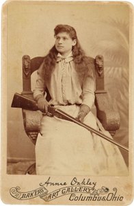 Annie Oakley: Hier sitzt die legendäre Scharfschützin eher schüchtern in einem massiven Renaissance-Stil Stuhl, ein Gewehr ruht auf ihrem Schoß. Ihre zarten weiblichen Züge und fließenden Haare täuschen über ihr robustes Outdoor-Image hinweg von American Photographer