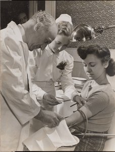 [Arzt und Krankenschwester setzen einer Frau eine Nadel ein]