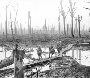 Fünf Australier, Mitglieder einer Feldartilleriebrigade, passieren einen Duckboard-Weg über Schlamm und Wasser zwischen kahlen Baumstämmen im verwüsteten Chateau Wood, einem Teil eines der Schlachtfelder