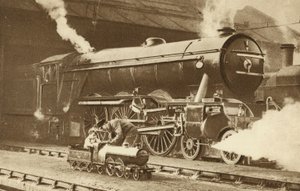 Junge reitet auf einer Spielzeug-Dampflokomotive vor dem echten Ding (s/w Foto) von English Photographer