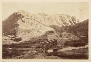Ansichten der Pazifikbahn, Eisenbahnschienen, die einen Fluss auf einer Fachwerkbrücke überqueren, mit Bergen dahinter von English Photographer