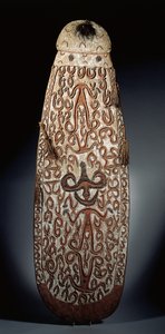 Ovaler Asmat-Schild, reliefartig geschnitzt mit scrollenden Ornamenten, die stark stilisierte Figuren einbeziehen, geflochtene Quasten am Rand von Guinean New