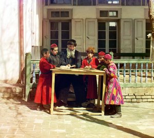 Eine Gruppe jüdischer Kinder mit einem Lehrer auf einem Tisch vor einem Haus, Samarkand, Russisches Reich, zwischen 1905 und 1915