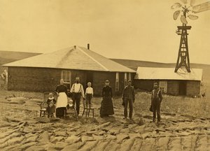 Familie von Siedlern vor ihrem Sodenhaus mit einer Windmühle auf dem Dach des angrenzenden Gebäudes in Custer County, Nebraska, ca. 1885 von Solomon D. Butcher