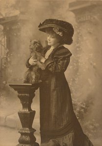 [Sarah Bernhardt in einem Studio, hält einen kleinen schwarzen Hund auf einem kunstvoll geschnitzten Holzsockel]