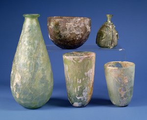 Im Uhrzeigersinn von links: birnenförmige grüne Glasflasche, Sassanidisch, 3.-7. Jahrhundert n. Chr.; hellbernsteinfarbene Glasschale, Sassanidisch, 5.-6. Jahrhundert n. Chr.; islamische grüne Glasbirnenflasche, ca. 8.-12. Jahrhundert n. Chr.; zwei islamis