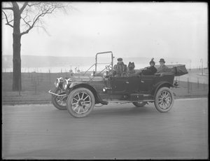 Drei nicht identifizierte Personen und zwei Chow-Hunde fahren in einem Cabriolet entlang eines Flusses oder Sees, ca. 1912