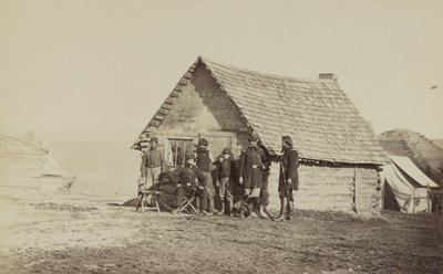 Eine Gruppe von Soldaten und zwei junge Männer, einer davon ein Afroamerikaner, stehen vor Blockhüttenquartieren, 1861-65 von American Photographer