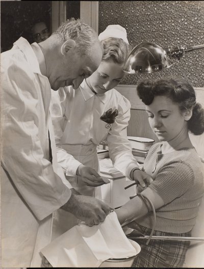 [Arzt und Krankenschwester setzen einer Frau eine Nadel ein] von Arnold Eagle