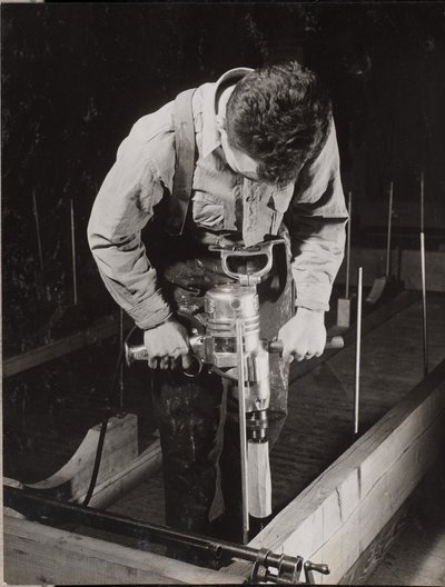 [Mann benutzt eine Handmaschine, um mit einem Stück Holz zu arbeiten] von Arnold Eagle