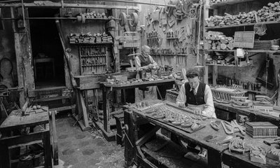 Handwerker an einer Werkbank in einer Werkstatt, die kleine Holzobjekte herstellen, die weder... von Bernard F. Rogers
