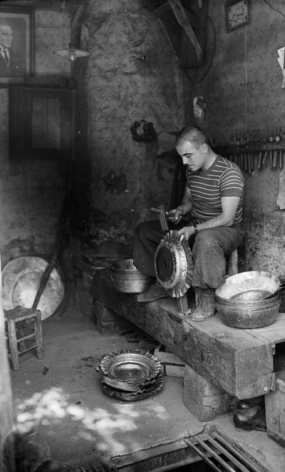 Italienischer Metallarbeiter hämmert auf ein Formblech, um ein erhöhtes Gefäß oder einen Topf herzustellen, Italien von Bernard F. Rogers