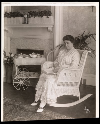 Mrs. Howard sitzt mit einem Buch in einem Schaukelstuhl in ihrem Haus in der 5th Avenue 200, New York, 1915-6 von Byron Company