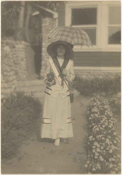 [Frau im Vorgarten mit Kamera und kariertem Regenschirm] von Louis Fleckenstein