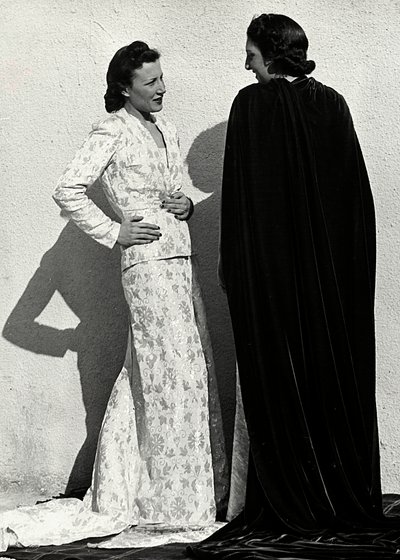 Zwei Modelle präsentieren Kreationen des italienischen Modehauses "Dragoni". Ein Modell trägt ein Outfit aus gemustertem Material, bestehend aus einer Jacke und einem langen Rock mit Schleppe. Das andere Modell, von hinten gesehen, trägt einen langen Samtu von Luis Bogino