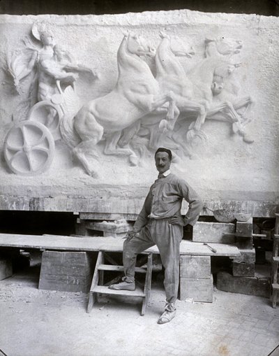 Ganzkörperporträt des berühmten Bildhauers Pietro Canonica. Er posiert in seinem Atelier vor einem Marmorhochrelief, an dem er arbeitet von Mario Nunes Vais