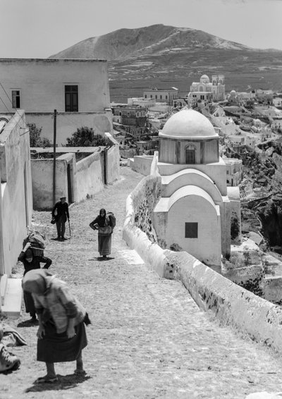 Griechische Dorfbewohner gehen eine Kopfsteinpflasterstraße in einem griechischen Dorf hinauf von Maynard Owen Williams