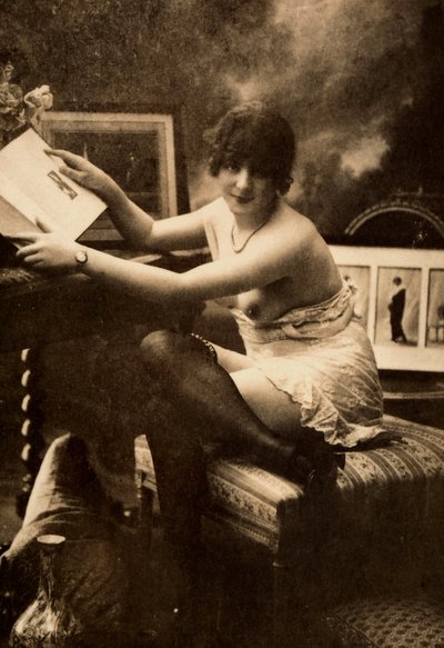 Porträt einer jungen Frau in intimer Kleidung, die an einem Tisch mit einem Buch sitzt von Unknown photographer