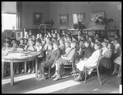 Kinder sitzen und hören im Lesesaal einer nicht identifizierten Filiale der Queens Borough Public Library zu, ca. 1910 von William Davis Hassler