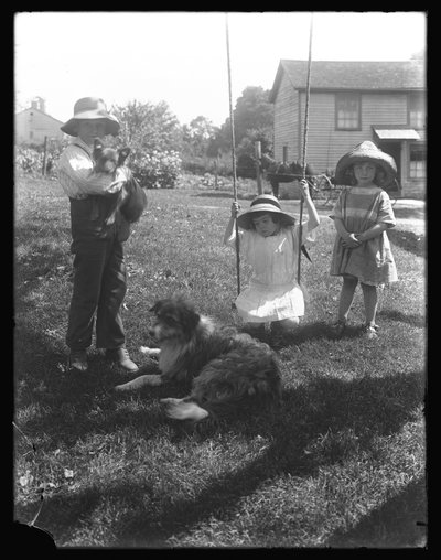 Kinder mit einem Hund und einem Welpen versammeln sich um eine Seilschaukel auf der McCready-Farm, Pennsylvania, ca. 1913 von William Davis Hassler
