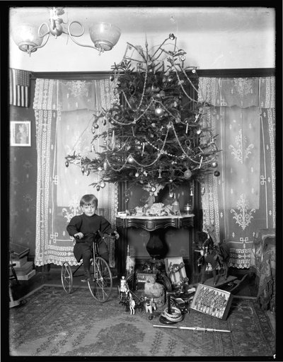 Seymour-Junge posiert sitzend auf Dreirad neben Weihnachtsbaum im Wohnzimmer, Weihnachten 1912 von William Davis Hassler