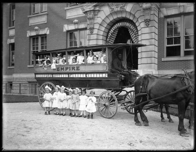 Kleine Mädchen posieren in und vor einem Pferdewagen, vor einem unbekannten Gebäude, wahrscheinlich das römisch-katholische Waisenhaus, Kingsbridge, Bronx, ca. 1910 von William Davis Hassler