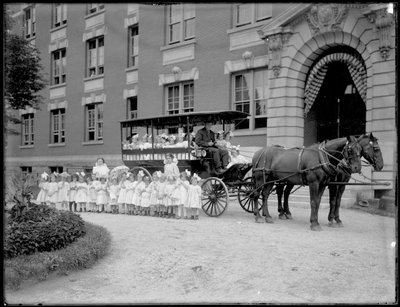 Kleine Mädchen posieren in und vor einem Pferdewagen, vor einem unbekannten Gebäude, wahrscheinlich das Römisch-Katholische Waisenhaus, Kingsbridge, Bronx, ca. 1910 von William Davis Hassler