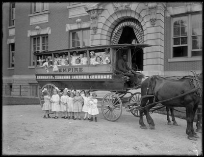 Kleine Mädchen posieren in und vor einem Pferdewagen, vor einem unbekannten Gebäude, wahrscheinlich das Römisch-Katholische Waisenhaus, Kingsbridge, Bronx, ca. 1910 von William Davis Hassler