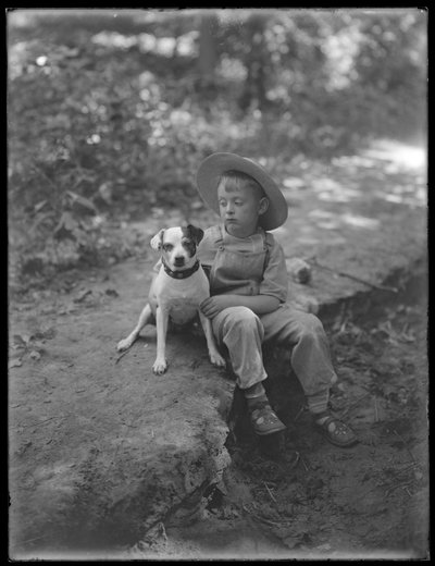 William Gray Hassler mit Strohhut und Latzhose, sitzend im Wald mit einem kleinen Hund (Bessie), 20. August 1911 von William Davis Hassler