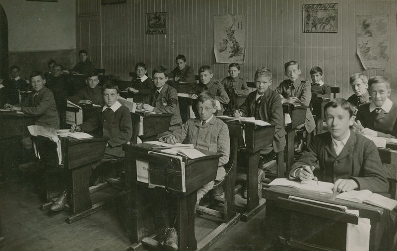 Männliche Schüler sitzen während einer Unterrichtsstunde an ihren Schreibtischen von English Photographer