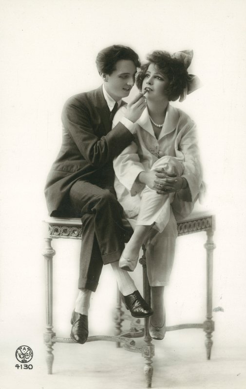 Androgyn Mann im Anzug, der Lippenstift auf die Lippen eines Mädchens im Pyjama aufträgt von French Photographer