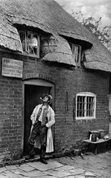 Ein Mann raucht eine Pfeife vor einem Geschäft, Worcestershire, um 1922