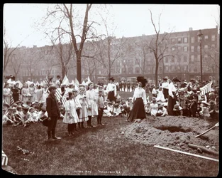 Erwachsene und Kinder mit Fahnen stehen um ein frisch gegrabenes Loch für eine Baumpflanzung am Arbor Day im Tompkins Square Park, New York, 1904